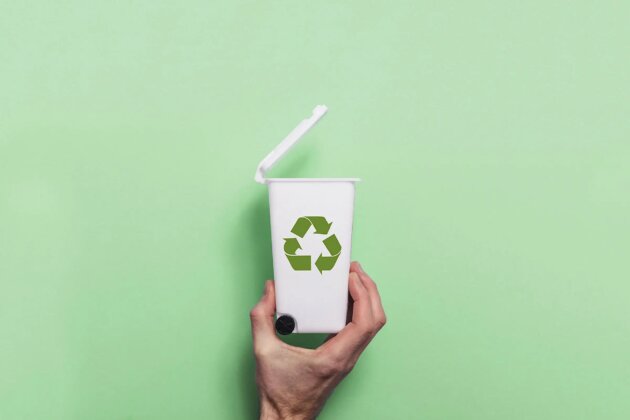 Hand holding recycling rubbish bin against a green background Hand holding recycling rubbish bin against a green background